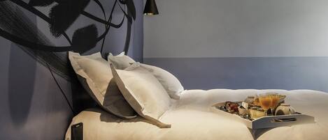 A modern bedroom with a neatly made bed, a bedside table with a lamp, and a tray with breakfast items.