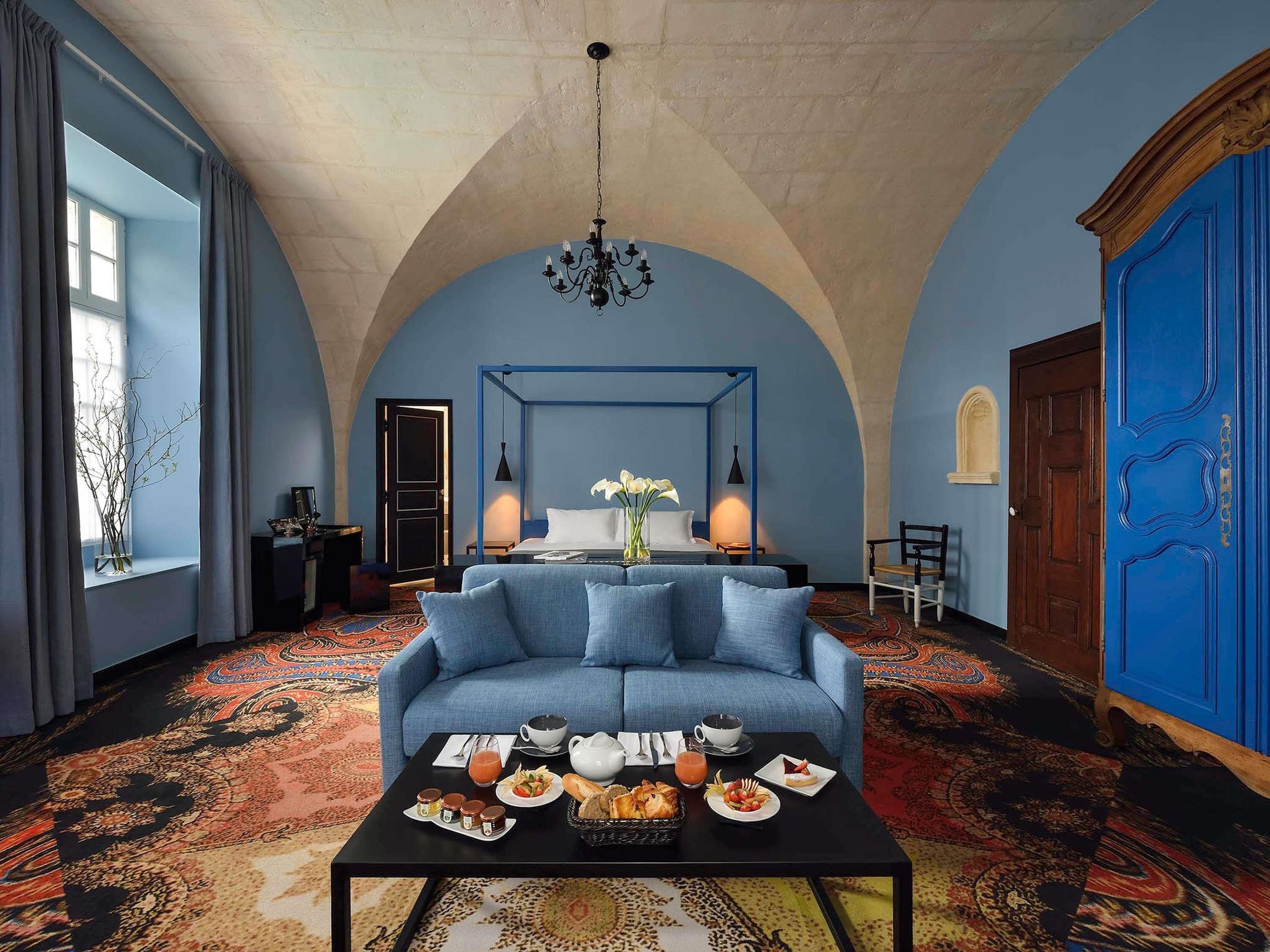 Ein Zimmer mit einem blauen Sofa, einem Couchtisch mit Frühstück, einer Chandelüster und einer blauen Tür.