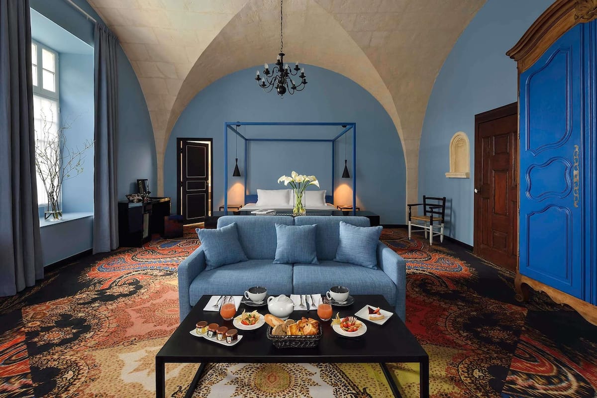 A room with a blue sofa, a coffee table with breakfast, a chandelier, and a blue door.