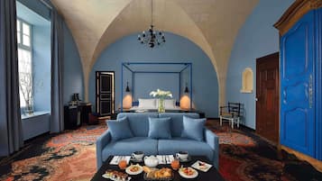Une pièce avec un canapé bleu, une table basse sur laquelle est servi le petit-déjeuner, un lustre et une porte bleue.