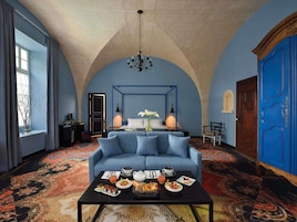 Una habitación con un sofá azul, una mesa de centro con desayuno, una lámpara de araña y una puerta azul.