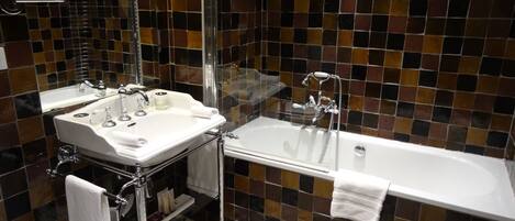 A bathroom with a white sink, mirror, and bathtub. The walls are tiled with a mosaic pattern.