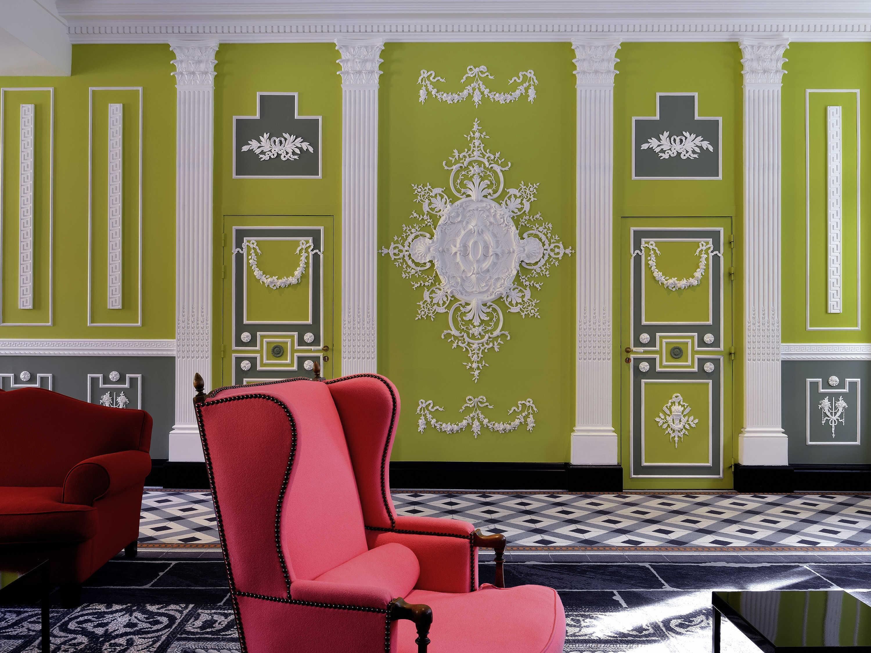 A room with green walls, white decorative moldings, a red armchair, and a patterned floor.
