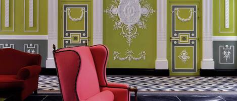 A room with green walls, white decorative moldings, a red armchair, and a patterned floor.