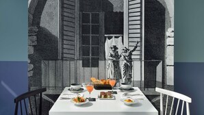 A dining table set with plates, glasses, and a basket of bread, with a view of a balcony and a building in the background. - Jules César Hotel & Spa Arles - MGallery Collection (Arles)