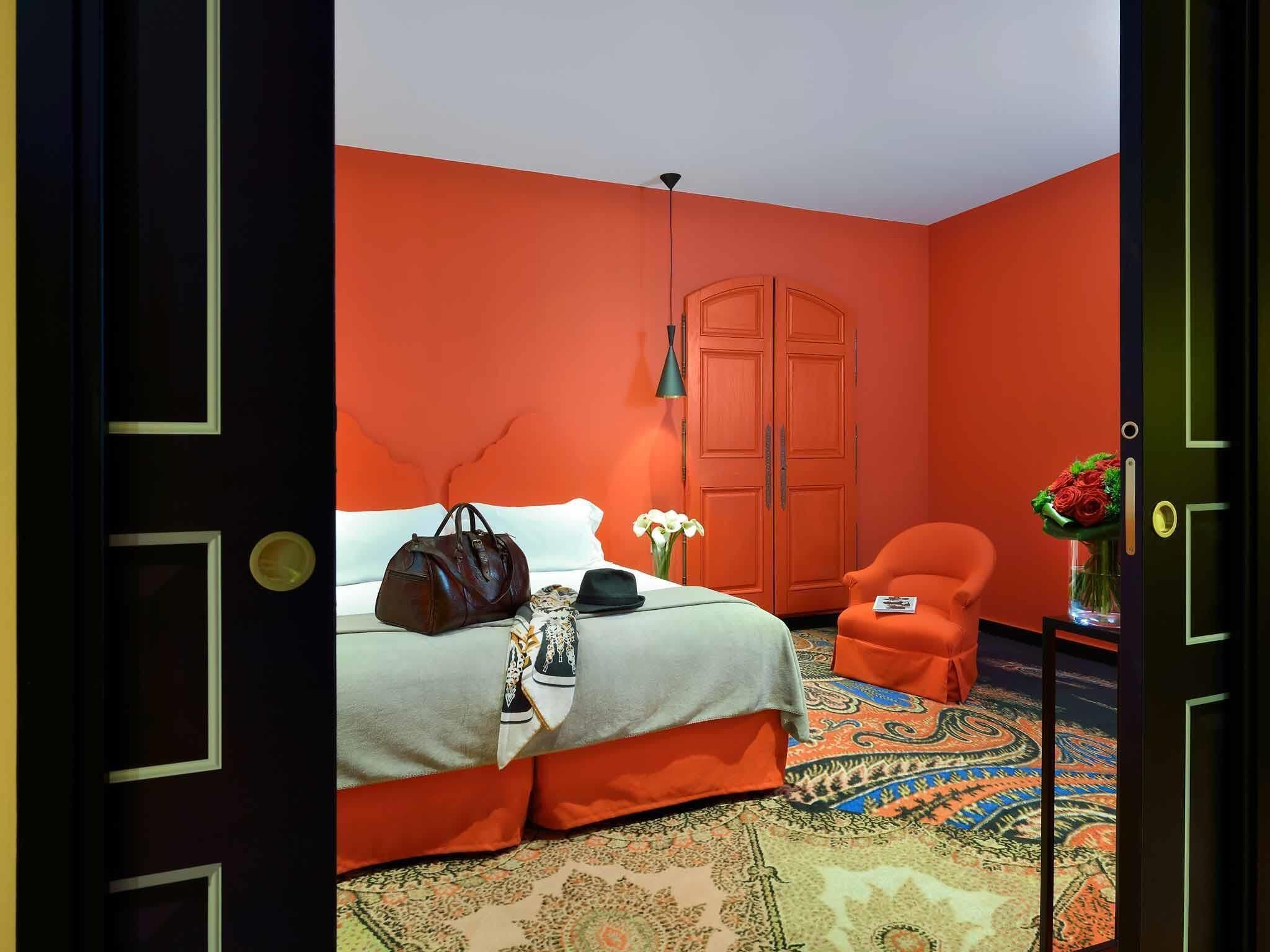 A room with a bed, a chair, a wardrobe, and a patterned rug.