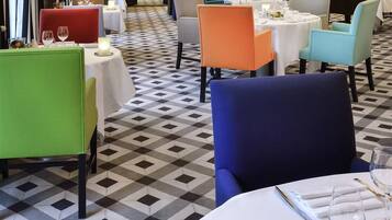 Comedor con mesas redondas, sillas de distintos colores y un piso con estampado de cuadros.