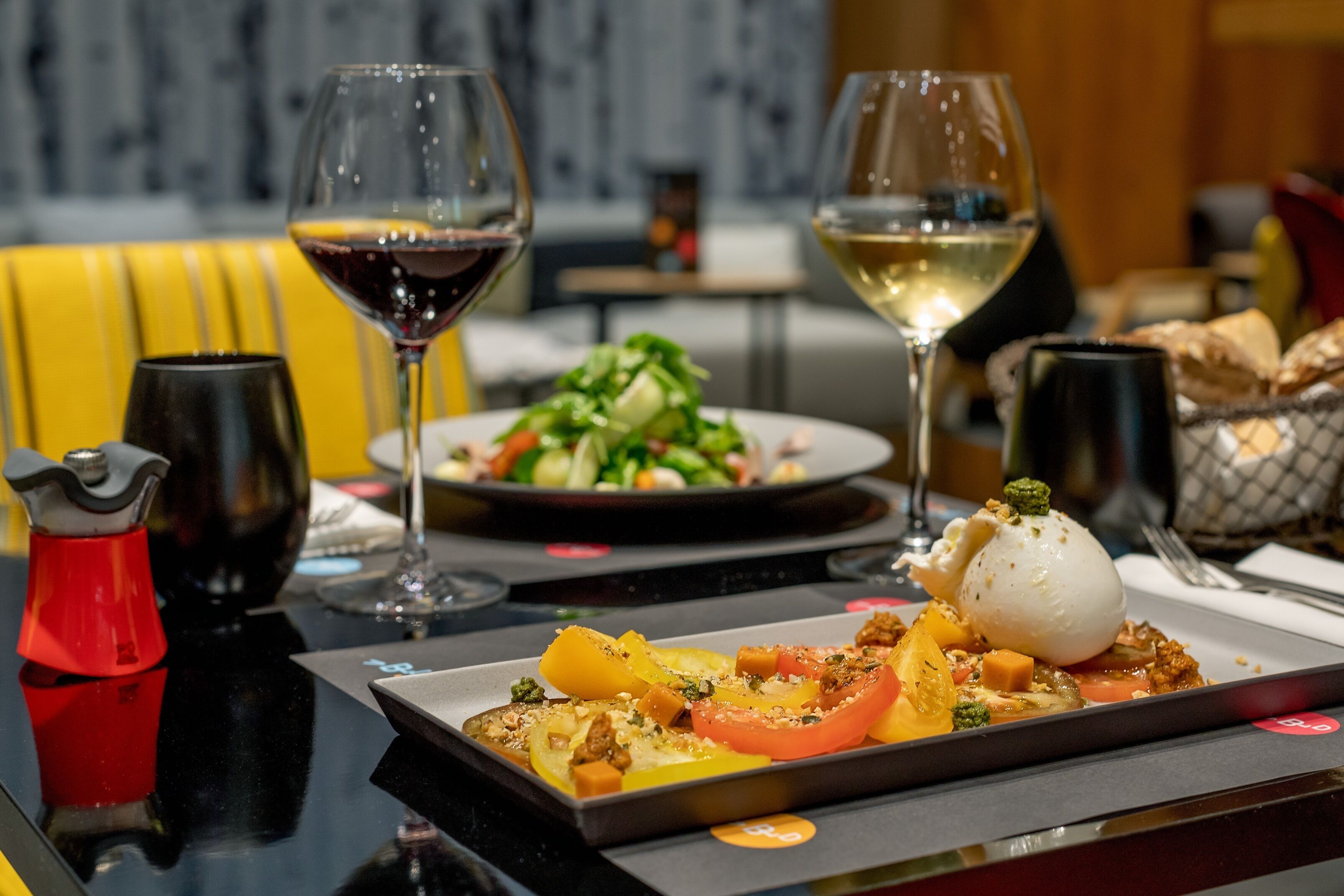 Een eettafel met een bord eten, twee glazen wijn en een rode zoutvaatje.