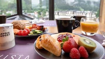 Una mesa de desayuno con cruasanes, fresas, frambuesas, kiwi y un vaso de jugo de naranja.