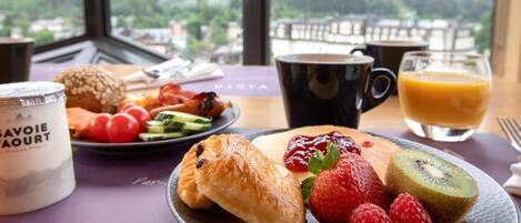 Una mesa de desayuno con cruasanes, fresas, frambuesas, kiwi y un vaso de jugo de naranja.