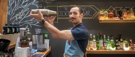 Un cantinero preparando una bebida en la barra, con estantes llenos de botellas de licor al fondo.