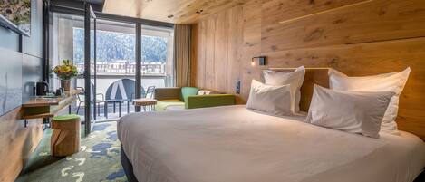 Habitación de hotel con una cama grande, un escritorio con silla, una mesita y vistas a una montaña y a la ciudad a través de un ventanal amplio.