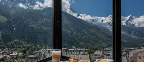 A table with breakfast items and a view of a mountain landscape through large windows.