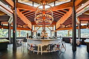 Un restaurante con barra central, vigas de madera en el techo y grandes ventanales con vistas a la montaña.