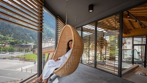 A person in a wicker chair by a large window overlooking a mountainous landscape. - Alpina Eclectic Hotel (Chamonix-Mont-Blanc)