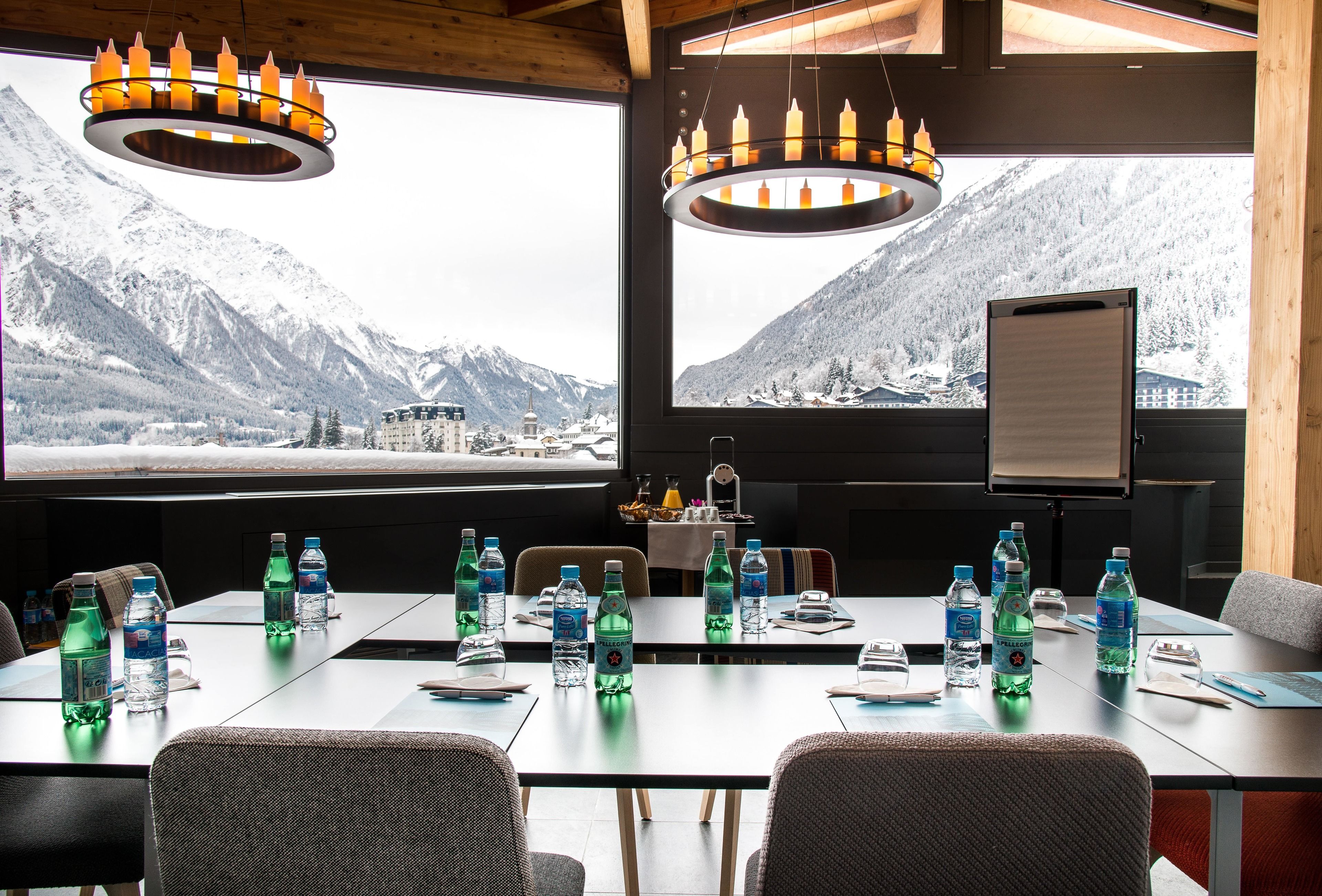 A conference room with a large table, chairs, water bottles, and a view of snow-covered mountains.