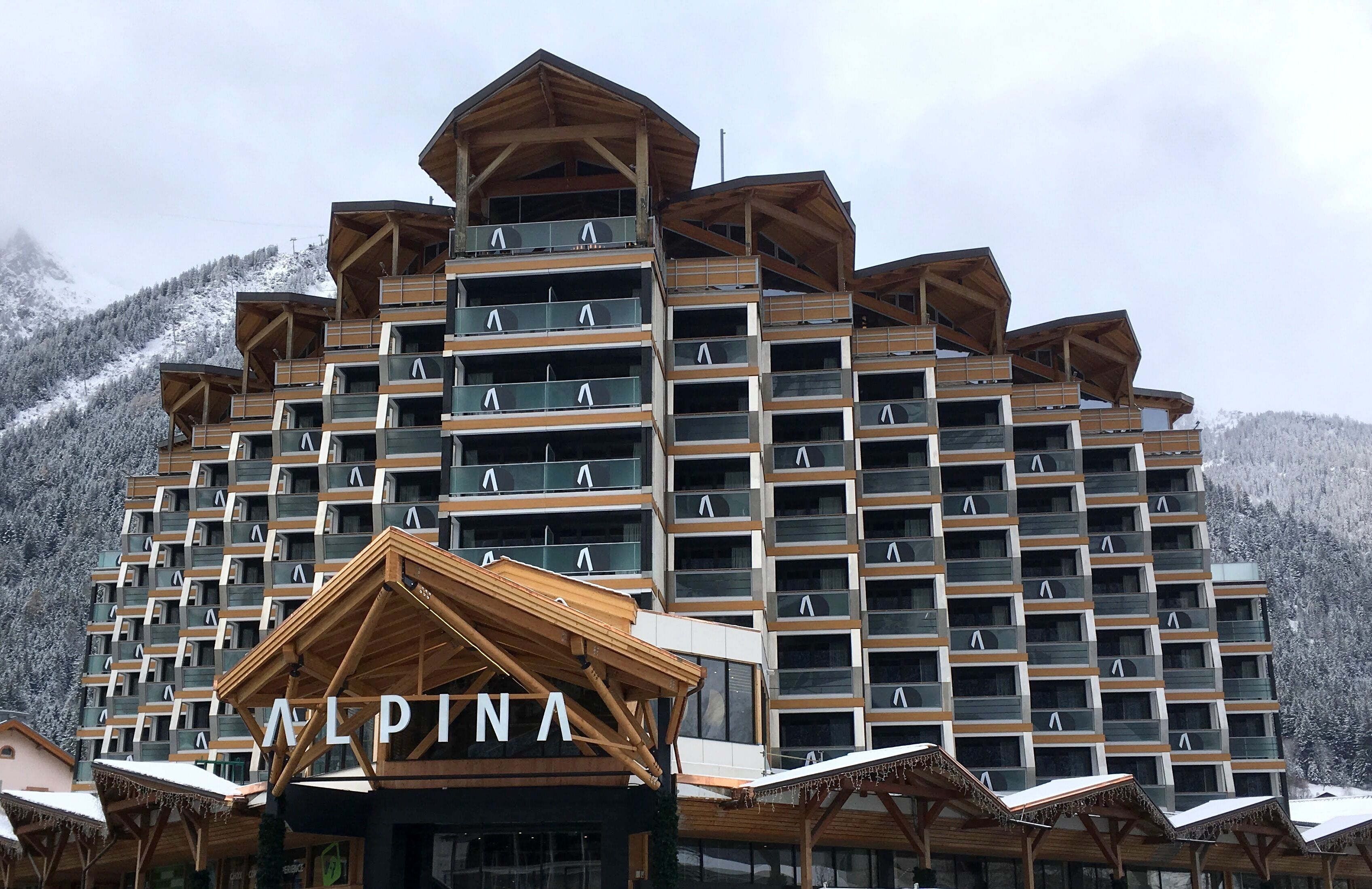 Un hotel a più piani con facciata in legno e balconi, circondato da montagne innevate.