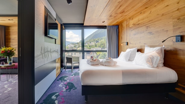 A modern hotel room with a large bed, a desk, and a view of the mountains. - Alpina Eclectic Hotel (Chamonix-Mont-Blanc)