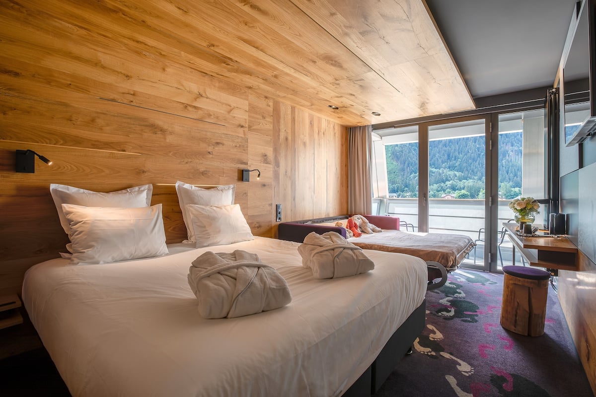 A wooden-paneled room with two beds, a desk, and a view of a mountainous landscape.