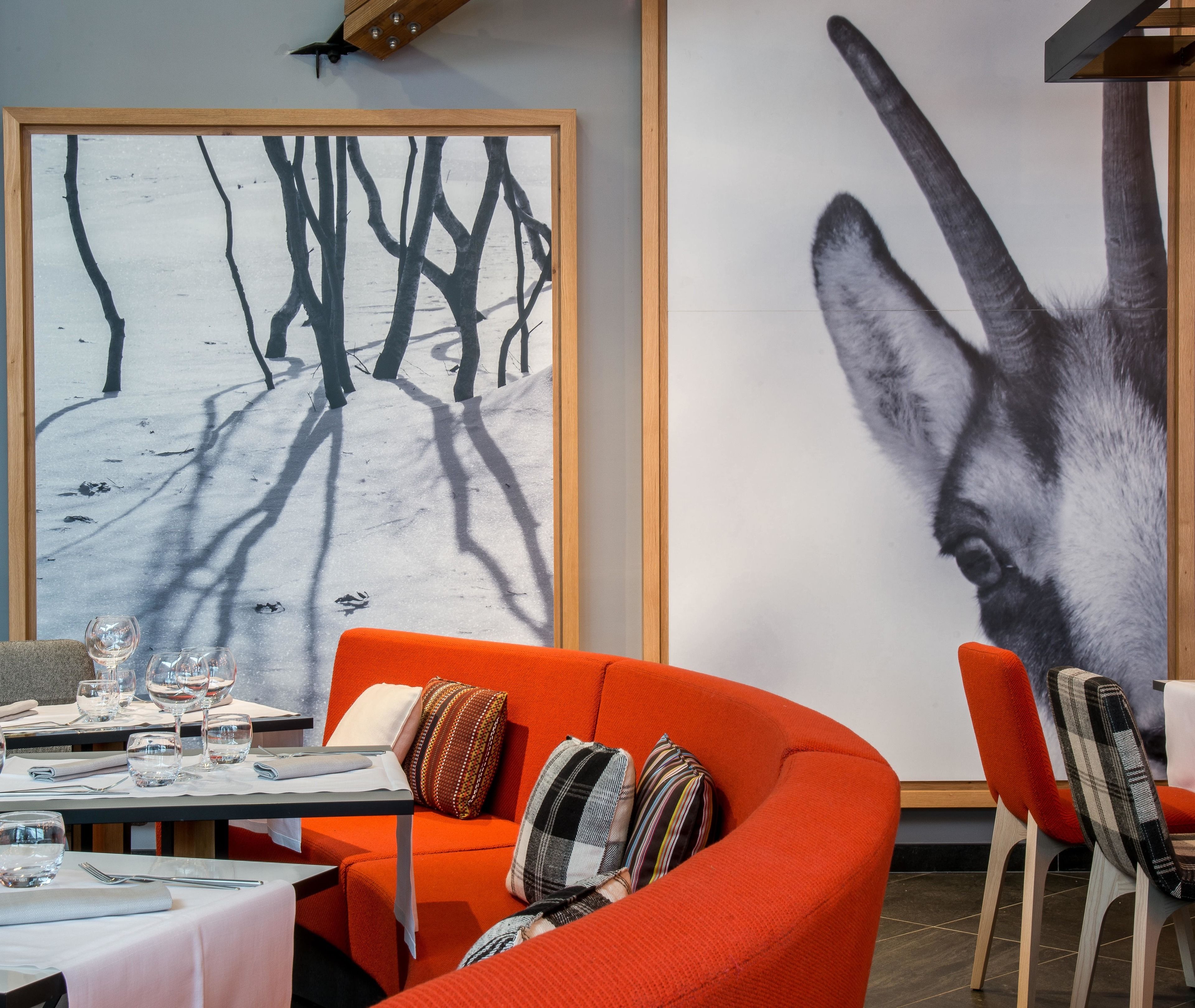 Un área de comedor con una mesa dispuesta para dos personas, un cuadro abstracto grande y un sofá naranja.