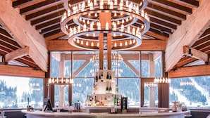 A bar with a circular chandelier, wooden beams, and a view of mountains through large windows. - Alpina Eclectic Hotel (Chamonix-Mont-Blanc)