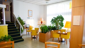Un vestíbulo de hotel con una escalera, sillas amarillas, una recepción y plantas en macetas.