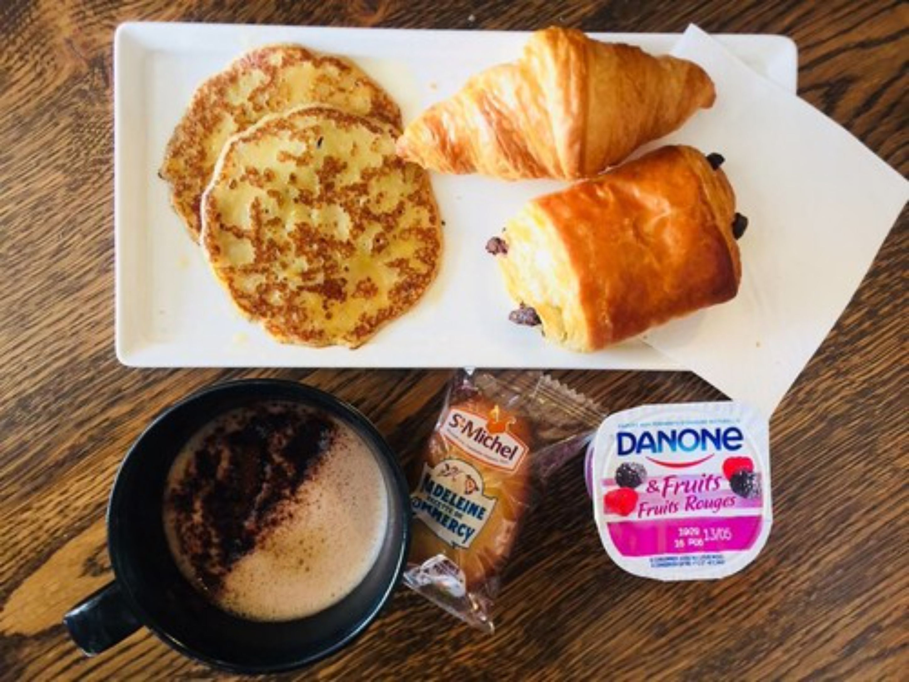 Un plato con tortitas, cruasanes y un envase de Danone.