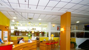 Zona de recepción de hotel con un mostrador curvo, una recepcionista y un área de estar con sillas y mesas.