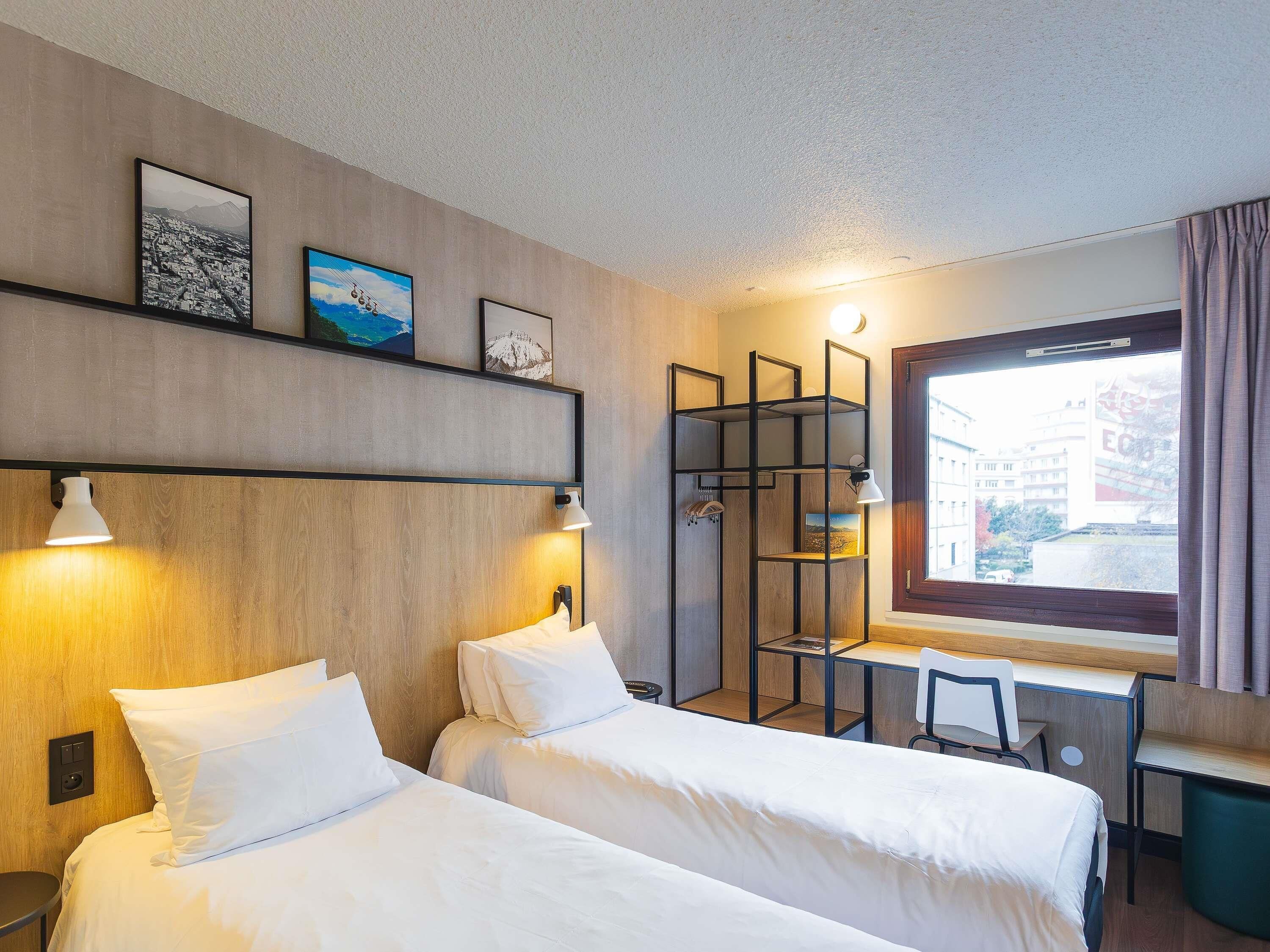 Une chambre d’hôtel avec deux lits, un bureau et une fenêtre avec des rideaux.