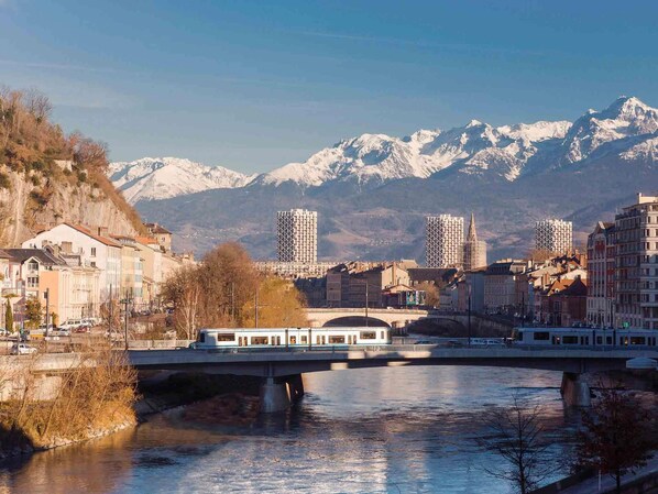 A river with a bridge, buildings, and snow-capped mountains in the background. - Ibis Grenoble Gare (Grenoble)