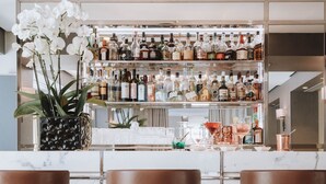 Un espace bar doté de comptoirs en marbre, de tabourets de bar en cuir marron et d’une variété de bouteilles d’alcool exposées sur des étagères.