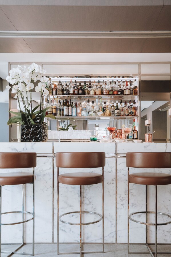 A bar area with marble countertops, brown leather bar stools, and a variety of liquor bottles on shelves. - Hôtel de Sers (Paris)