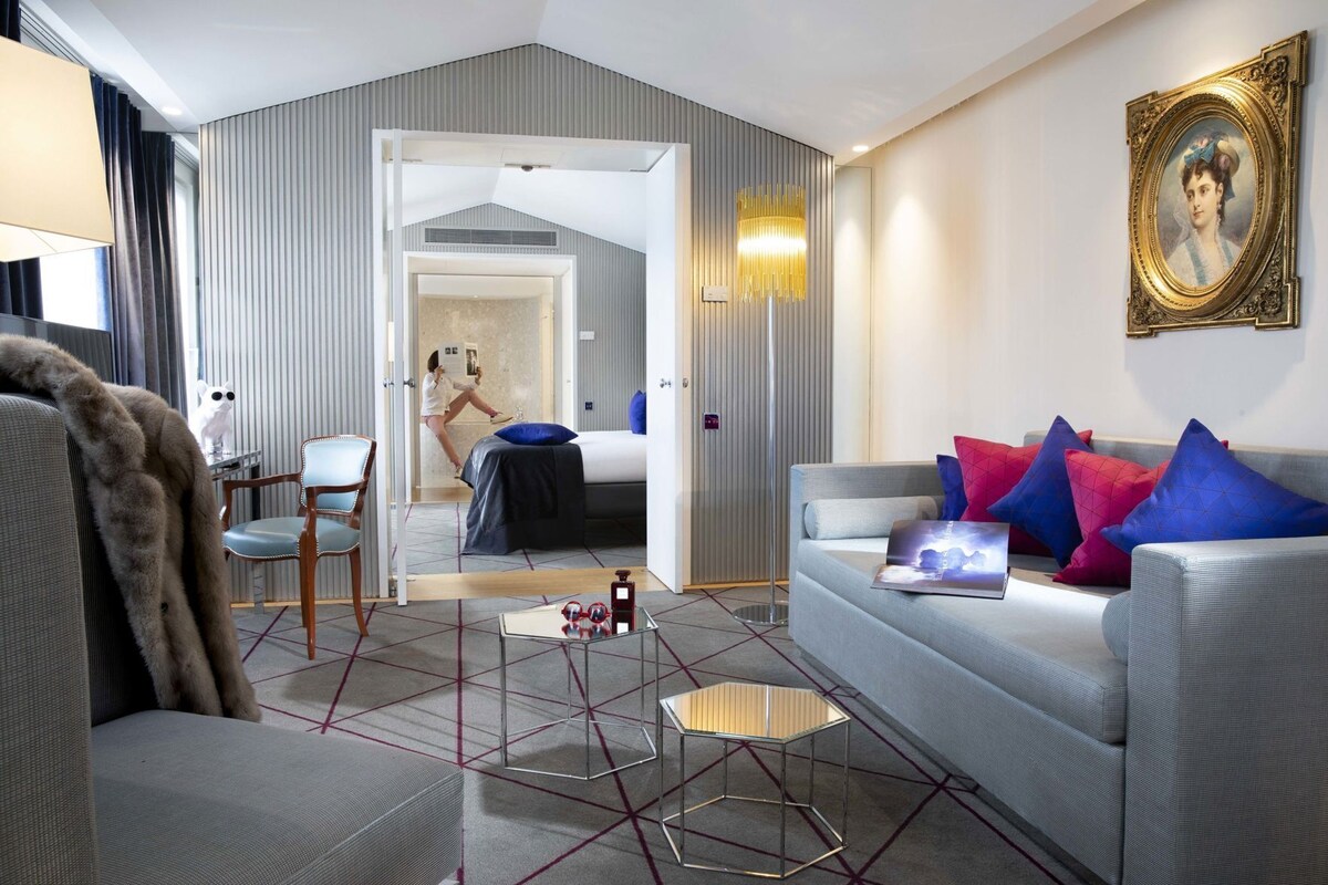 A modern hotel room with a grey sofa, a coffee table, and a painting on the wall.