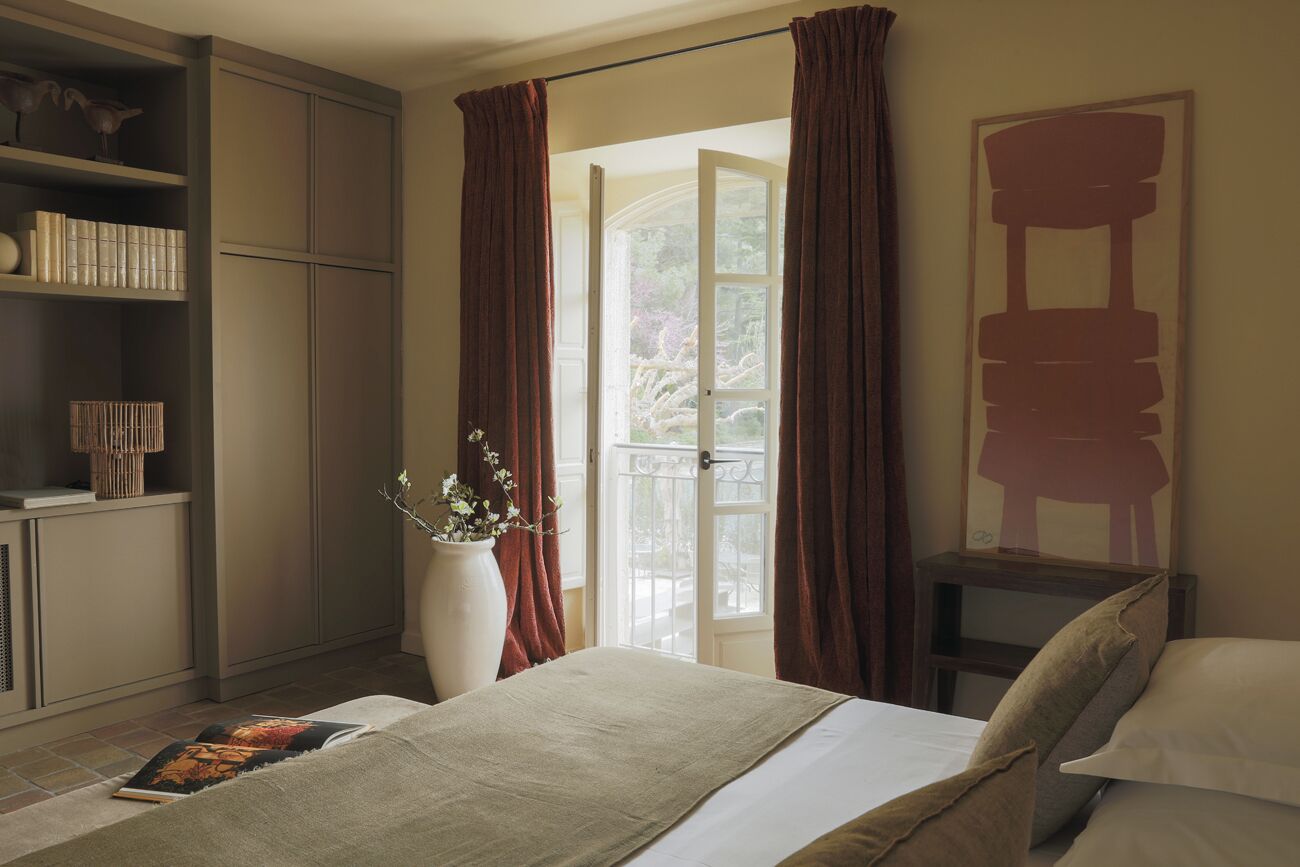 Un dormitorio con cama, estantería, un florero con flores y vistas a través de una puerta.