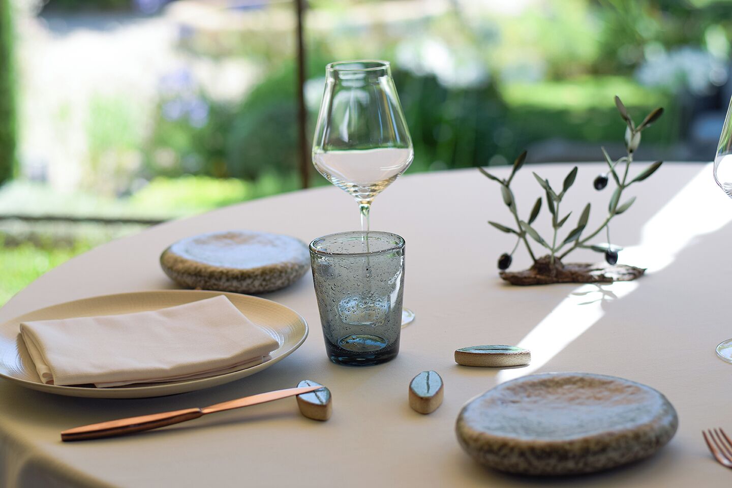 A table set with a glass of white wine, a napkin, cutlery, and coasters.