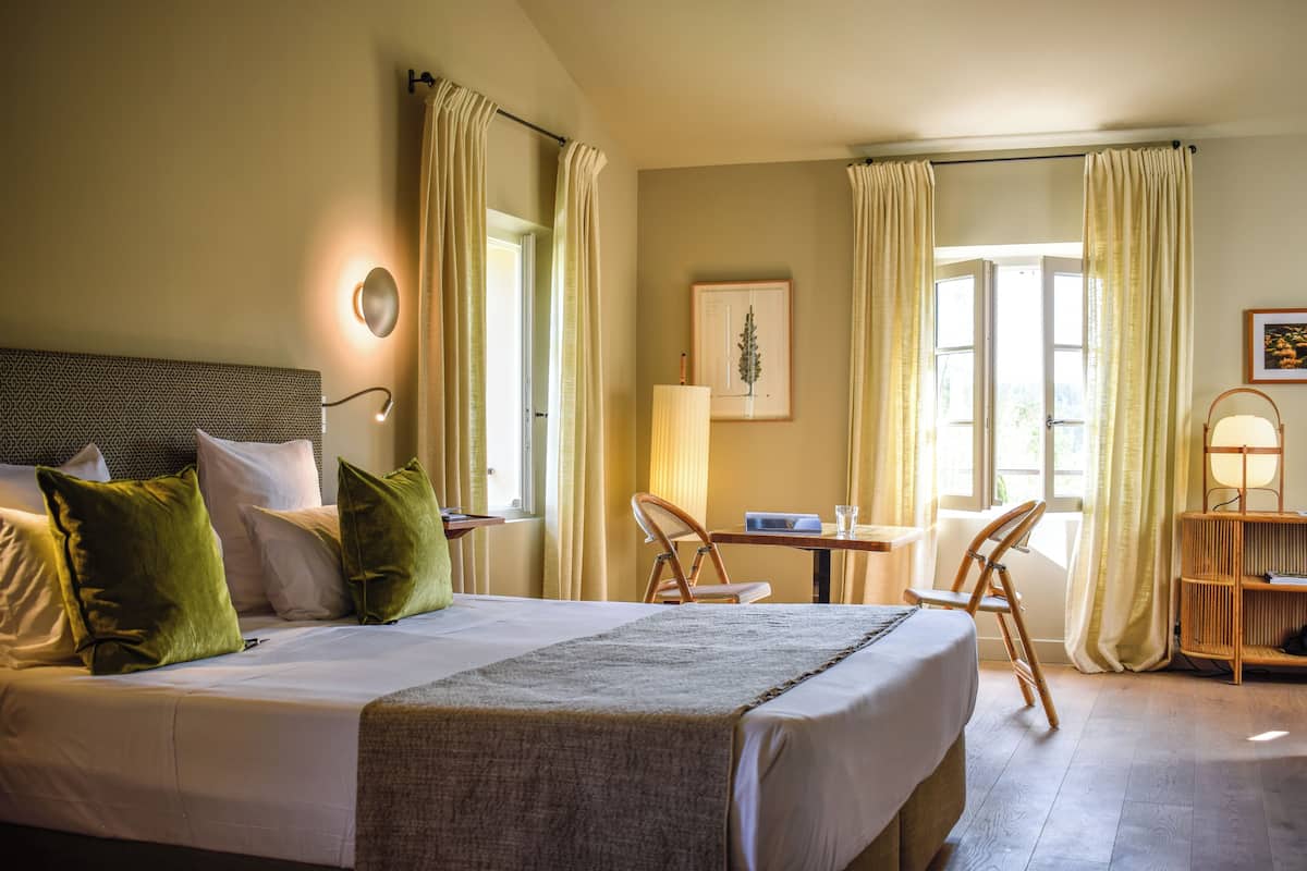 A hotel room with a large bed, a desk, two chairs, a lamp, and a picture on the wall.