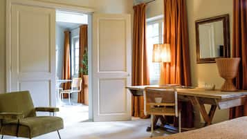 A hotel room with a desk, two chairs, a lamp, a mirror, and a bed.