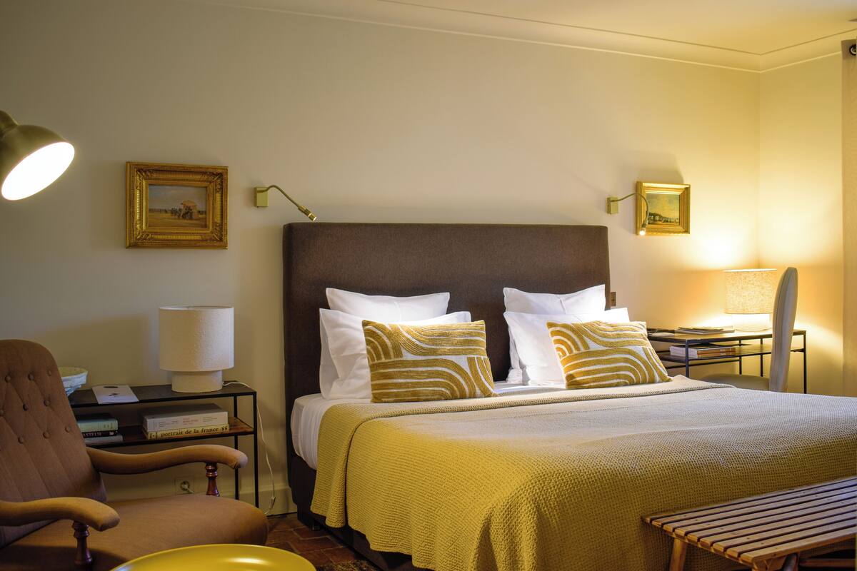 A neatly arranged hotel room with a bed, a chair, a bedside table, and a lamp.