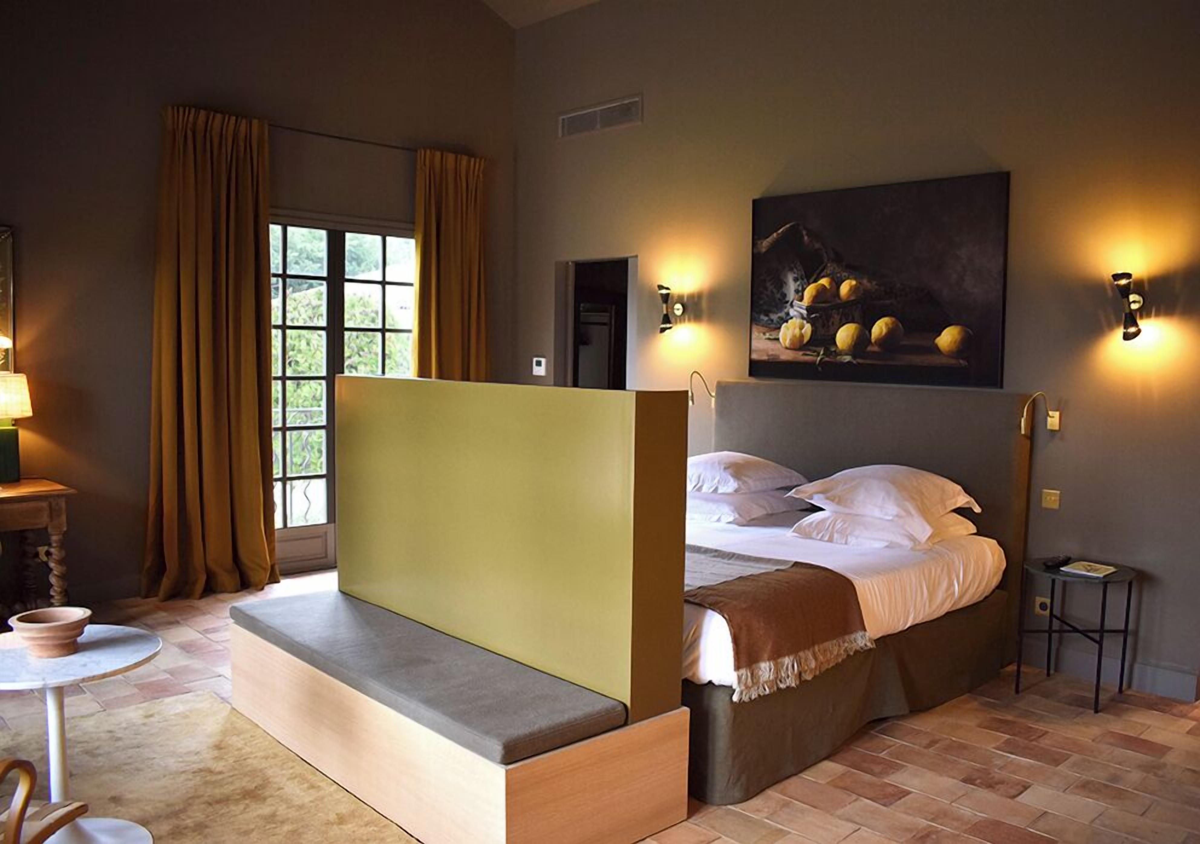 A bedroom with a bed, a bench, a table, and a painting.