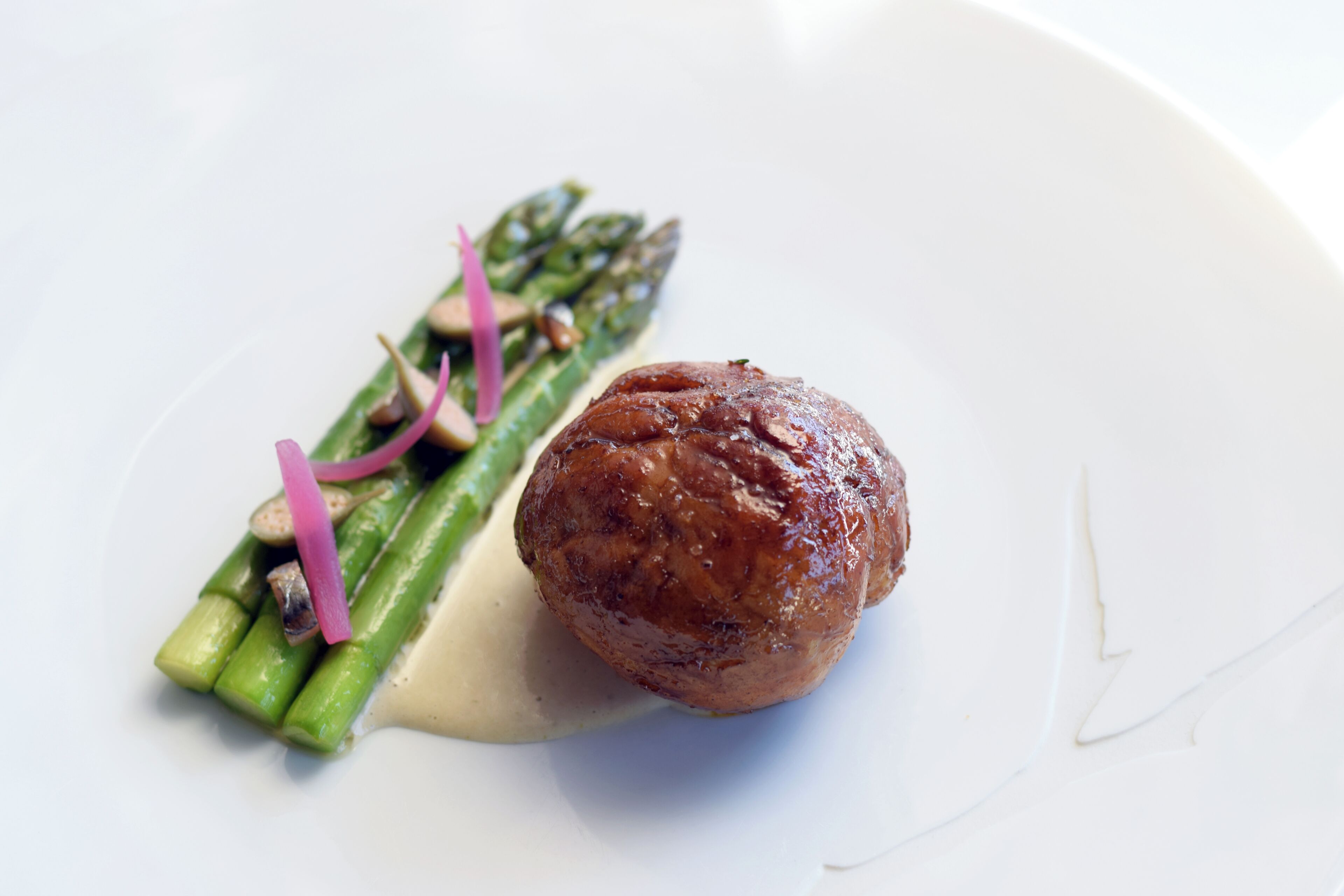 A white plate with a round meat, green asparagus, and a creamy sauce.