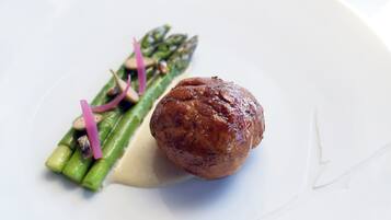 A white plate with a round meat, green asparagus, and a creamy sauce.
