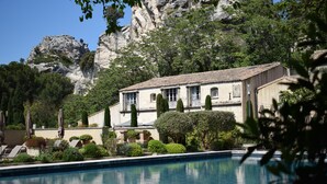 A pool with a building in the background, surrounded by greenery and a rocky cliff.
