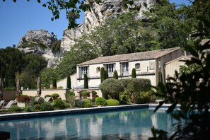 Ein Pool mit einem Gebäude im Hintergrund, umgeben von viel Grün und einer Felswand.