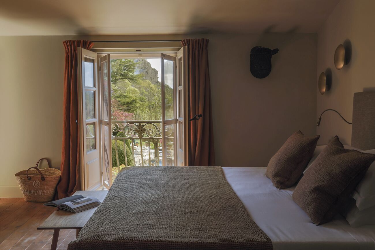Un dormitorio con cama, ventana con cortinas, balcón e iluminación fijada a la pared.