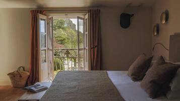 Un dormitorio con cama, ventana con cortinas, balcón e iluminación fijada a la pared.