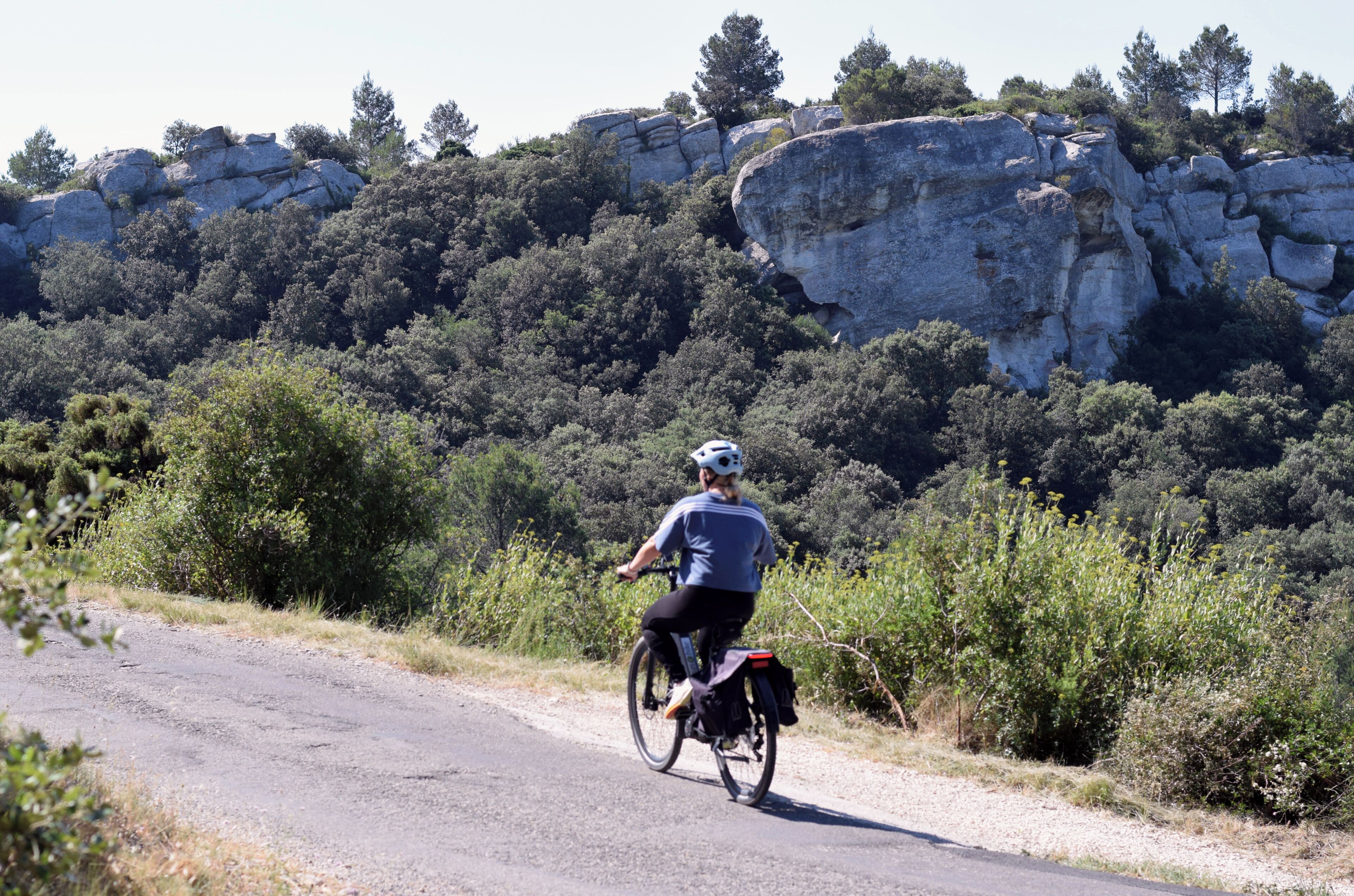A person riding a bicycle on a road with a rocky hillside and trees in the background.