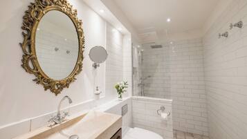 A bathroom with a large ornate mirror, a sink, a toilet, and a shower area.