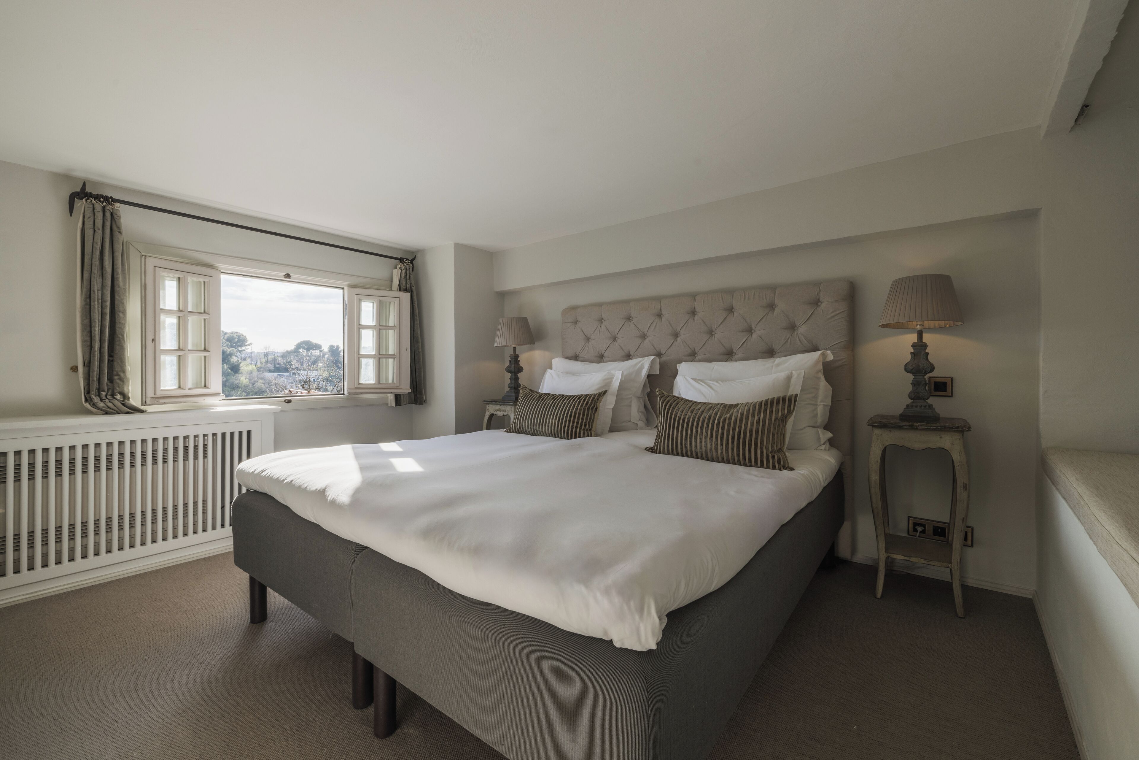 Een slaapkamer met een groot bed, twee nachtkastjes, een raam met gordijnen en een radiator.