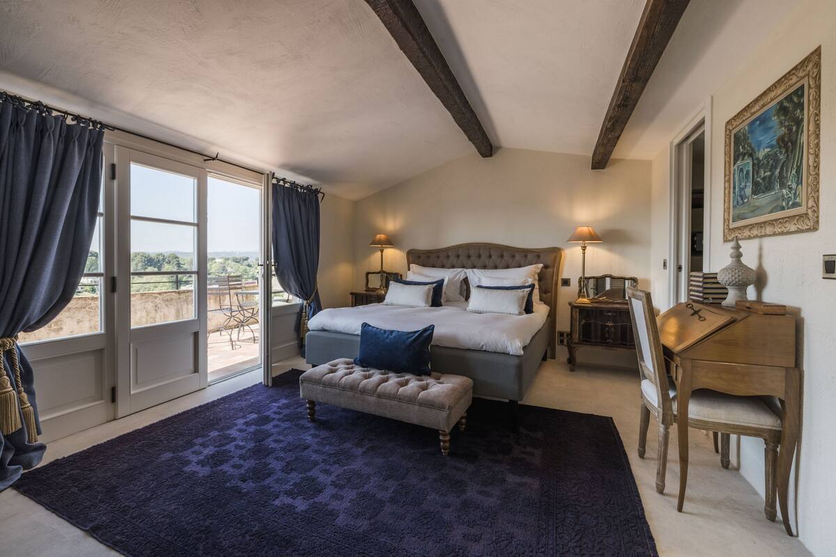 A bedroom with a large bed, a bench, a desk, and a chair.