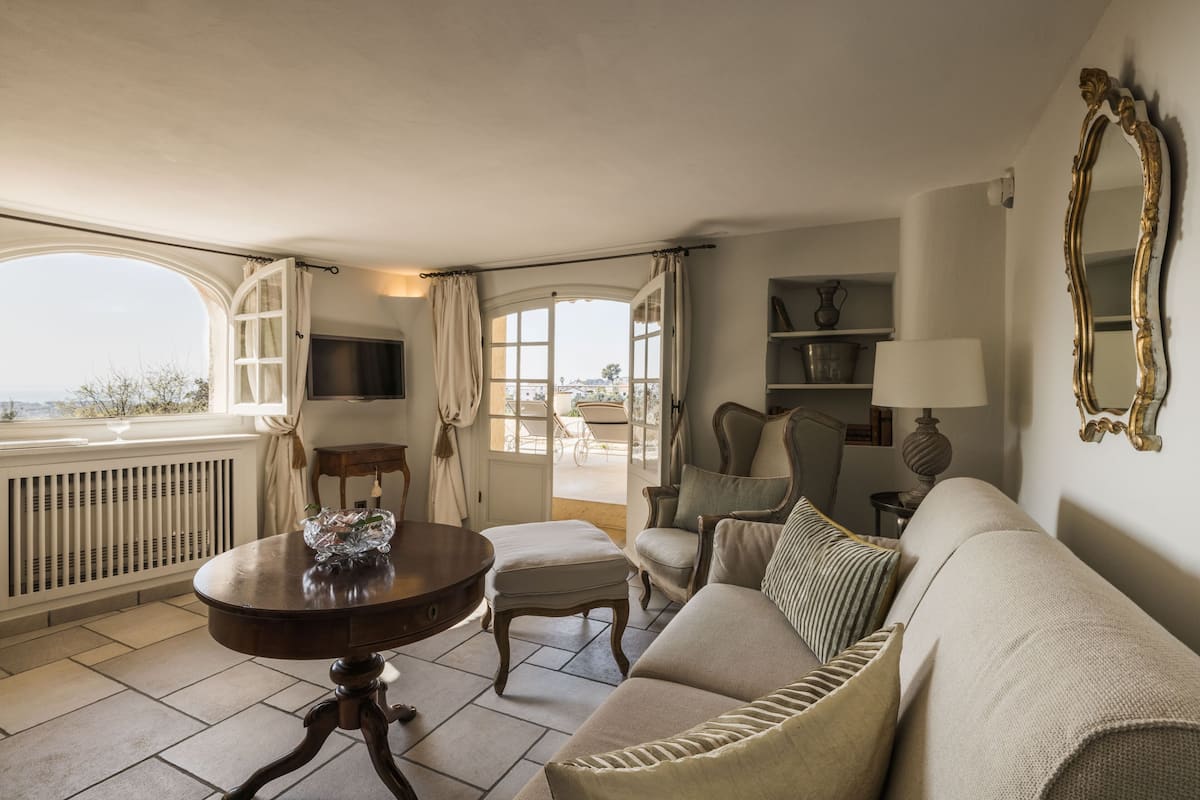A room with a sofa, a table with a decorative item, a chair, a lamp, a mirror, and a view through a window.